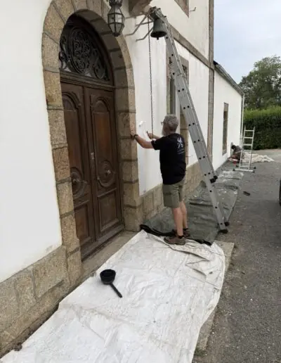 Volunteer rolling fresh white paint beside a carved wooden door during a mission painting project with PDV France