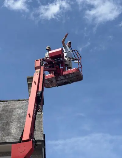 Two volunteers waving from a raised boom lift after a day of painting for PDV France