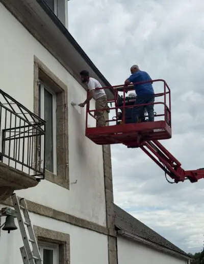 Volunteers painting an upper exterior wall from an aerial lift during a mission trip with PDV France