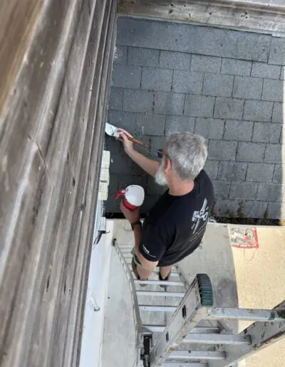 Volunteer brushing white paint onto exterior trim from a ladder during a mission project in France